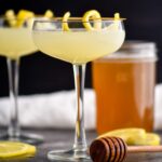 two glasses of bees knees cocktail with honey syrup and lemon twist garnish