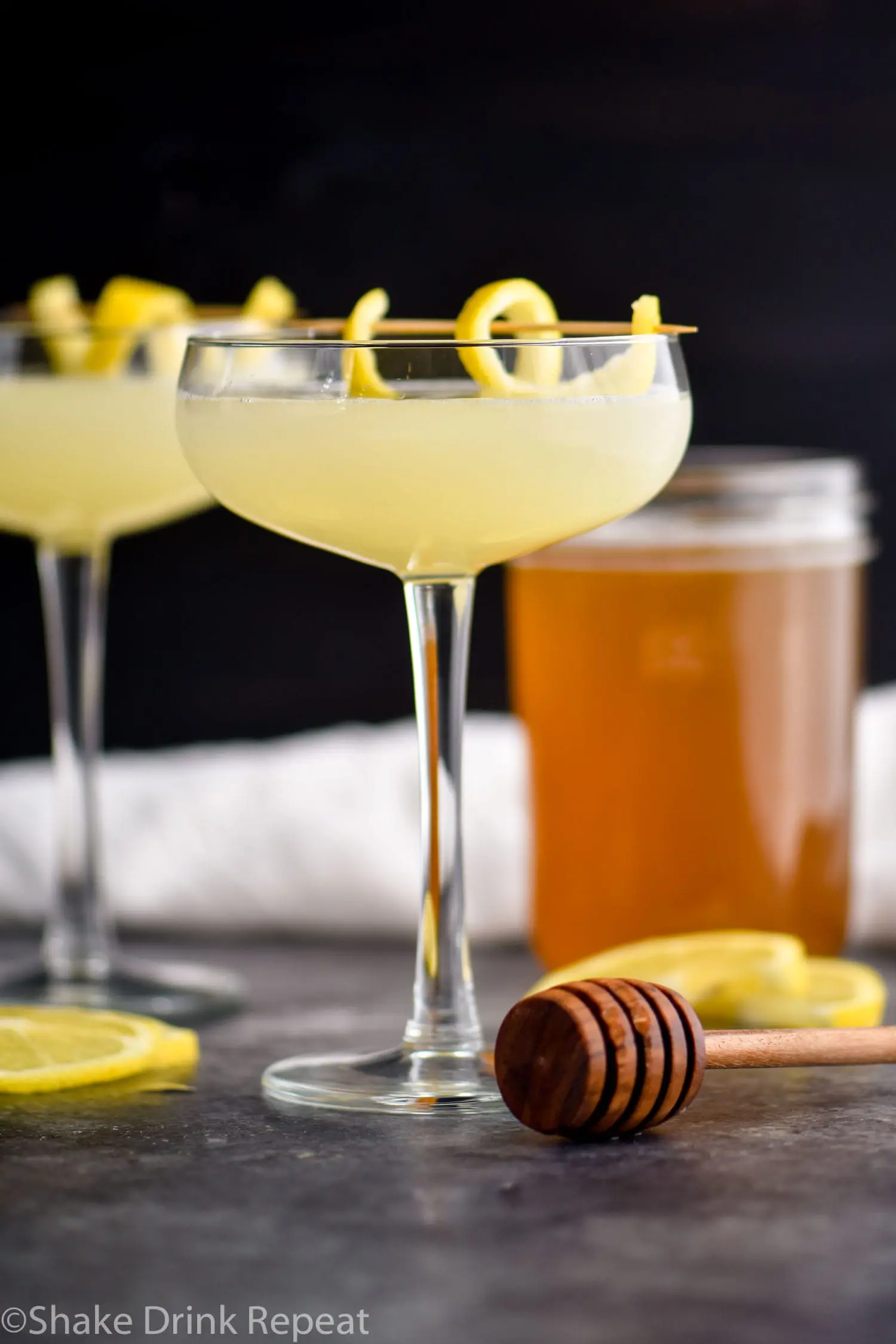 two glasses of bees knees cocktail with honey syrup and lemon twist garnish