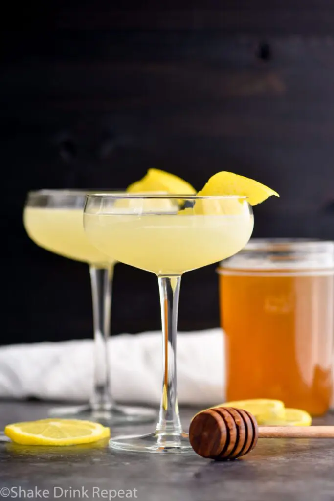 two glasses of bees knees cocktail with lemon and honey syrup