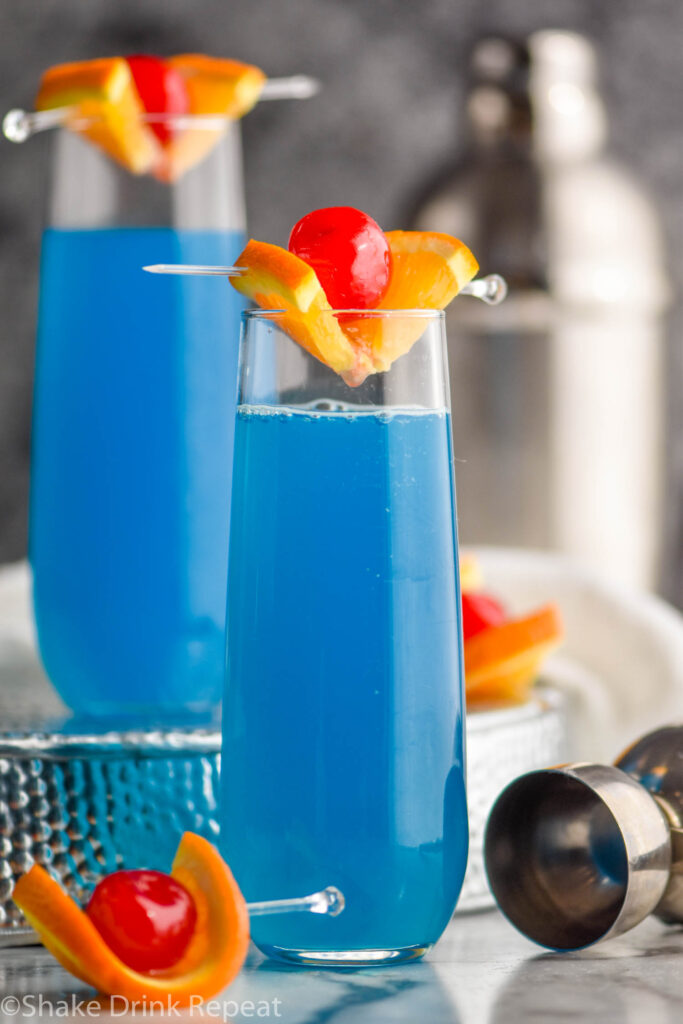 two glasses of blue kamikaze cocktails with orange and cherry garnish