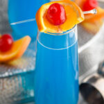 glass of blue kamikaze cocktail with orange and cherry garnish