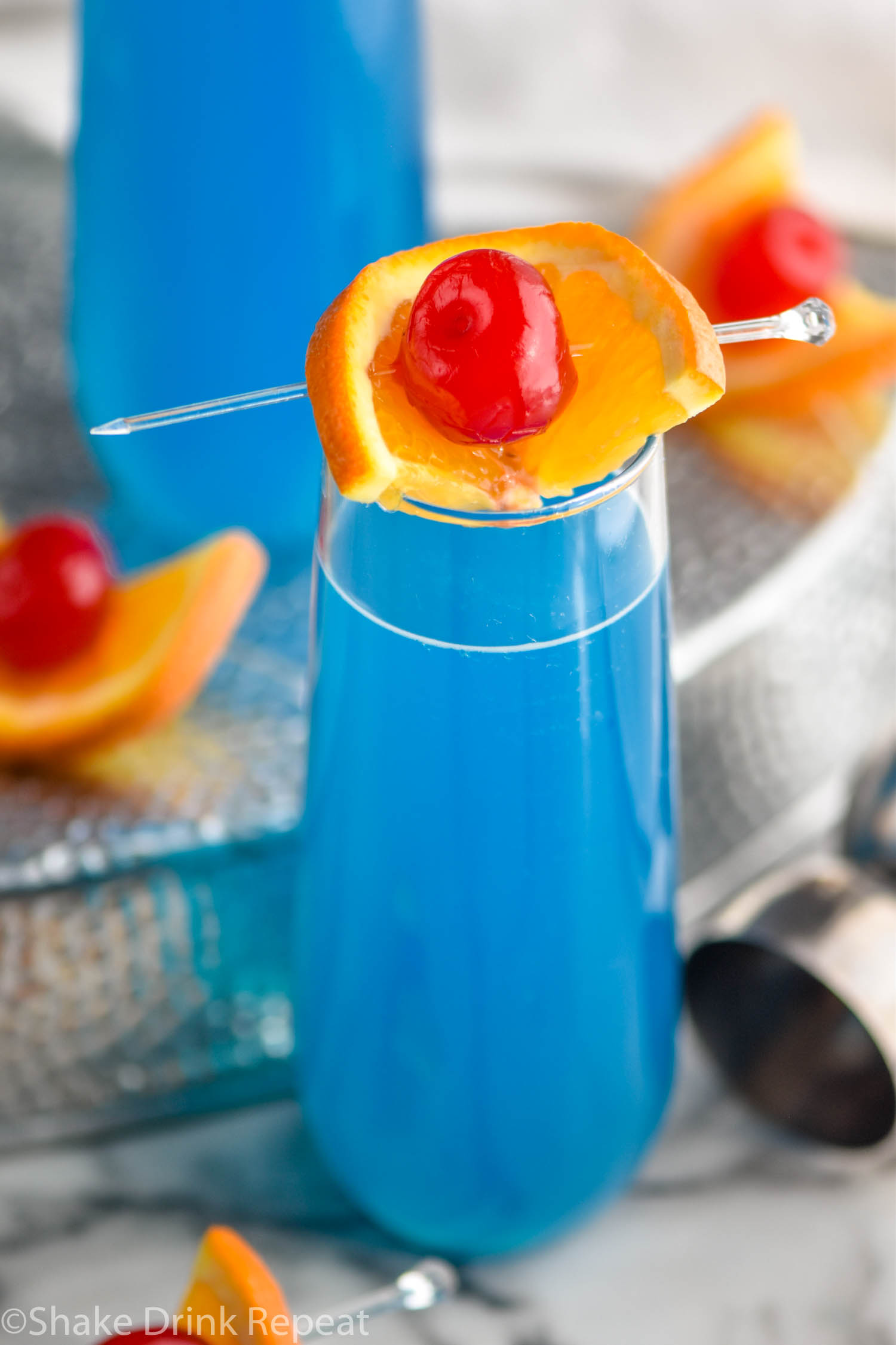 glass of blue kamikaze cocktail with orange and cherry garnish
