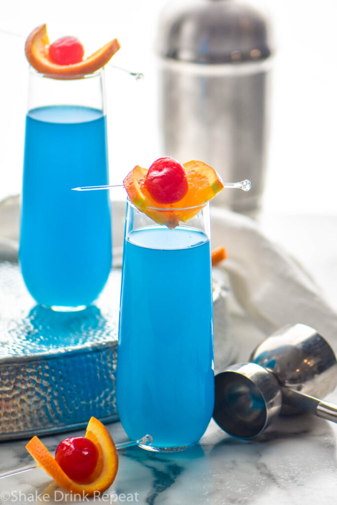 two glasses of blue kamikaze with orange and cherry garnish