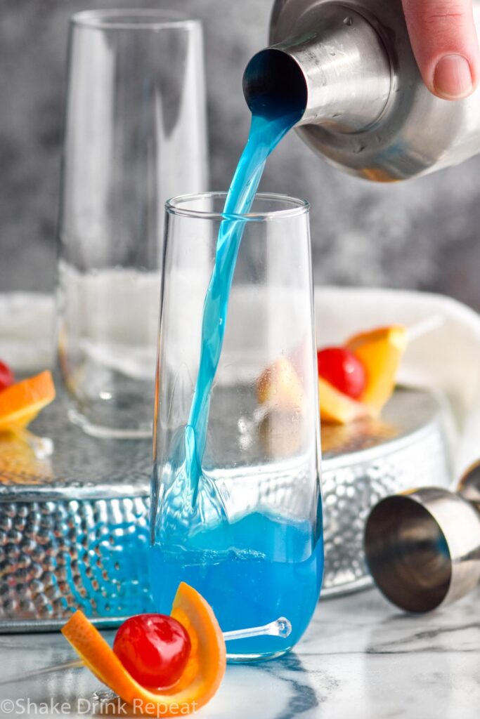 making glass of blue kamikaze with orange and cherry garnish