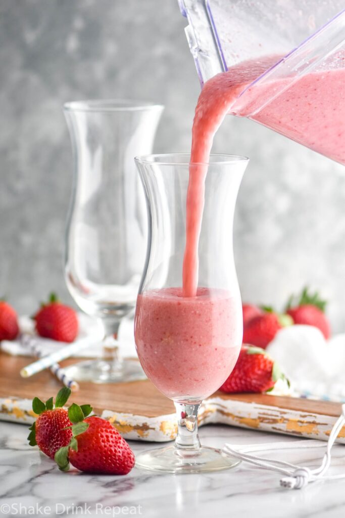 Bunny Colada being poured into a glass, strawberries and straws around it