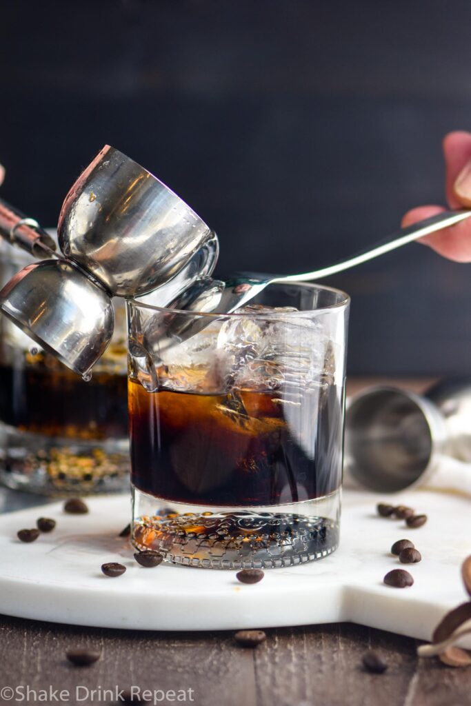 making a mind eraser cocktail in a glass with ice, jigger, vodka, coffee liqueur and spoon