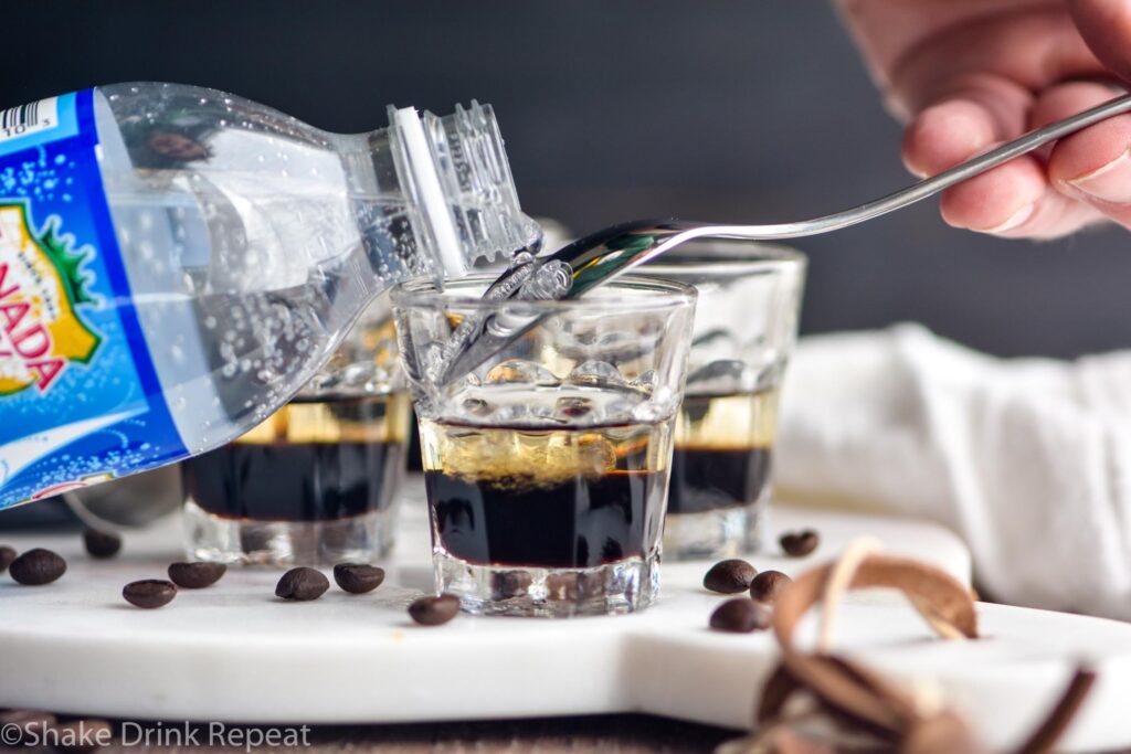 making glass of mind eraser shot with club soda water being poured over spoon for layers