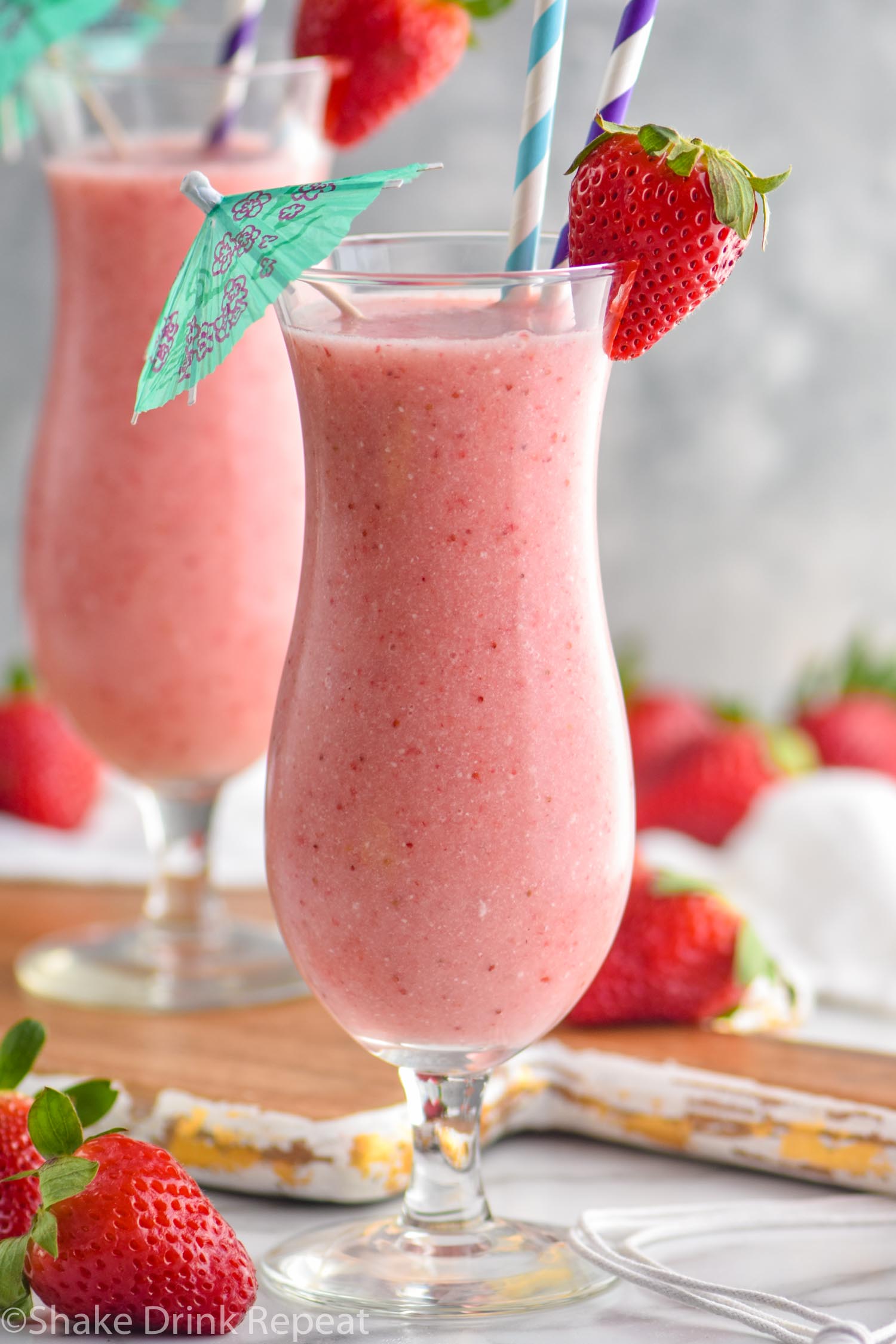 two glasses of strawberry colada drink with straws and umbrella