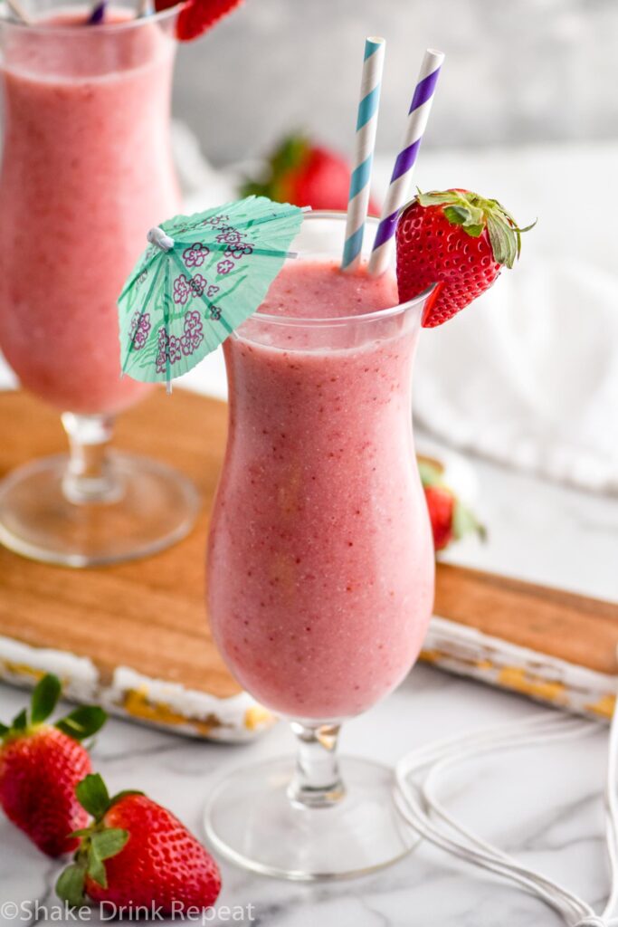 two glasses of strawberry colada cocktail with straws and umbrella