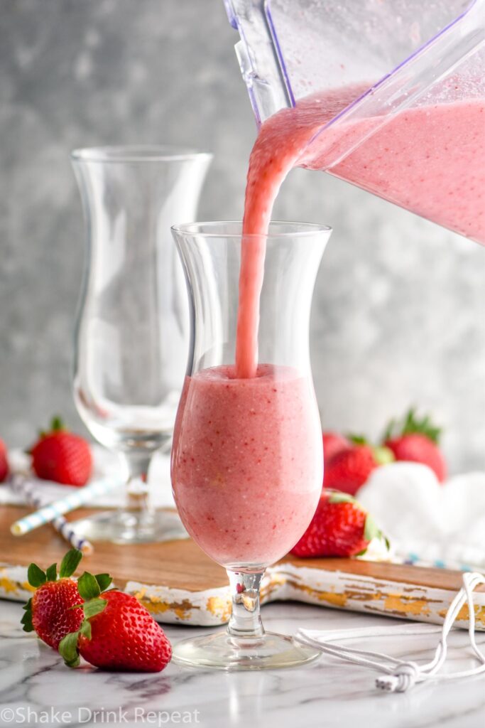 pouring strawberry colada recipe into glass surrounded by fresh strawberries