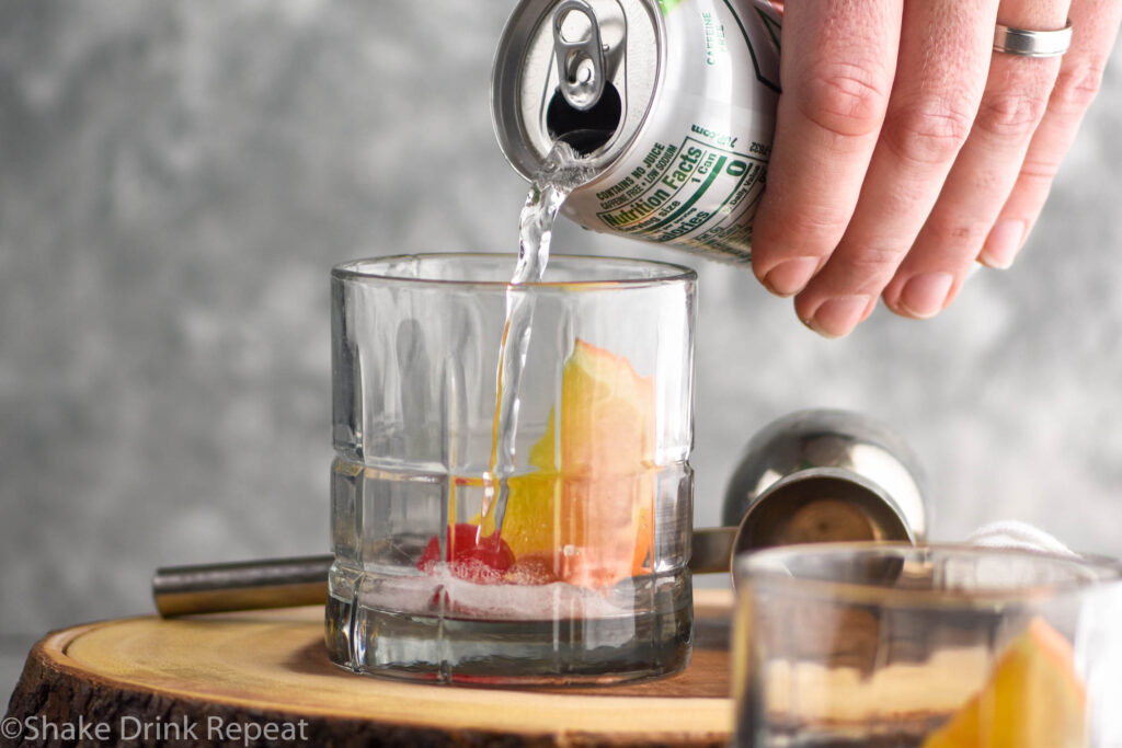 glass of wisconsin brandy old fashioned ingredients with ice, sugar cube, cherry, orange, and lemon-lime soda