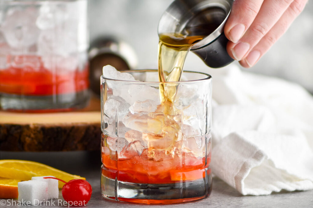 glass of wisconsin old fashioned ingredients with ice, sugar cube, brandy, cherry, and orange