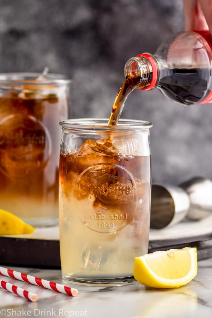 Man pouring ingredients into a glass of long island iced tea with ice, lemon and cola