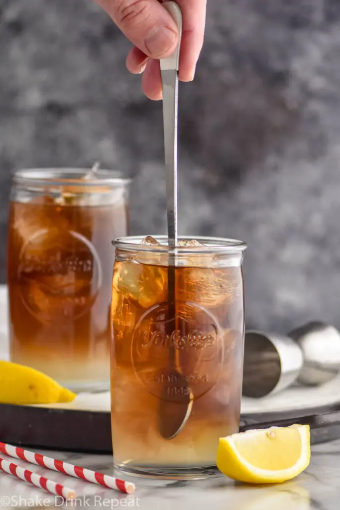 man stirring a glass of long island iced tea with ice and lemons