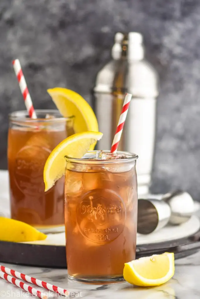 two glasses of long island iced tea with ice, straws, and lemon garnish