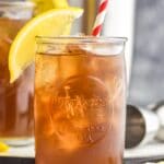 two glasses of long island iced tea with ice, a straw and lemon garnish