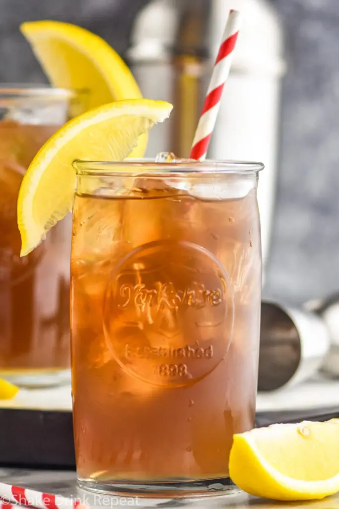 two glasses of long island iced tea with ice, a straw and lemon garnish