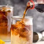 pouring cola into a glass of long island iced tea with ice and lemon