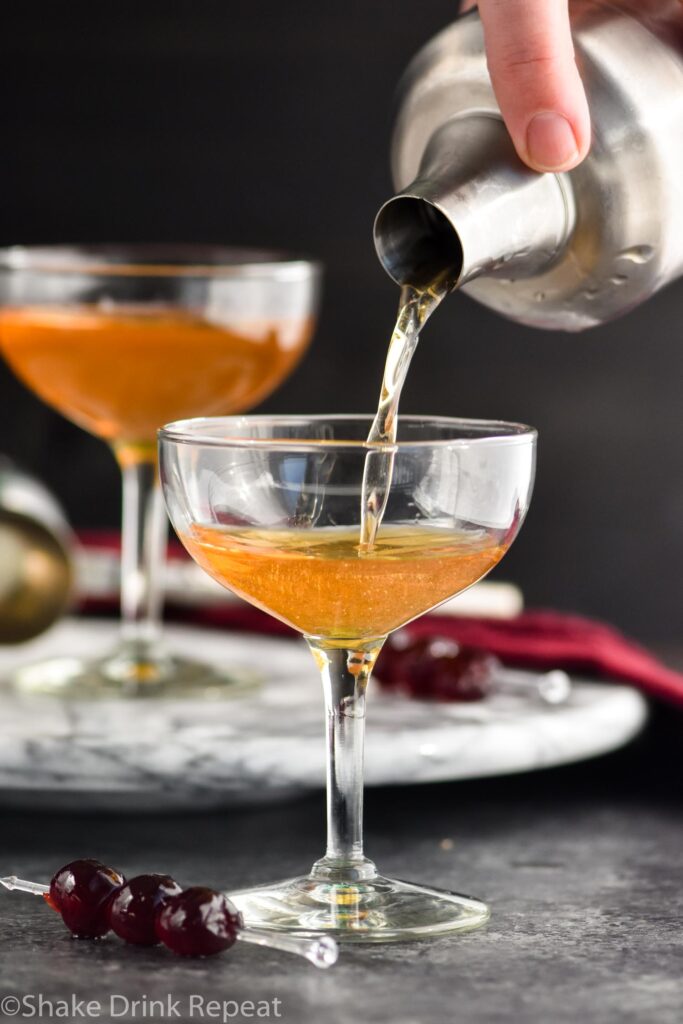 Making a Manhattan cocktail and pouring into a glass with cherry garnish