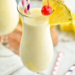glass of pina colada with straws, pineapple wedge, and cherry