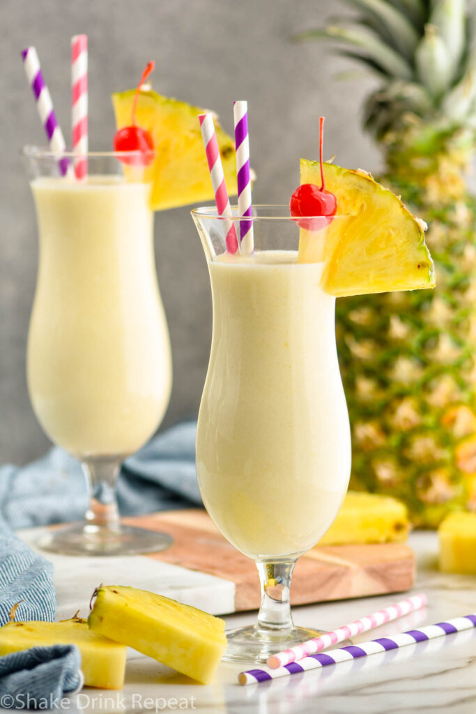 two glasses pina colada with straws, pineapple wedge, and cherry