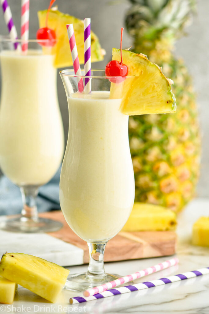 two glasses of pina colada with straws, pineapple wedge, and cherry