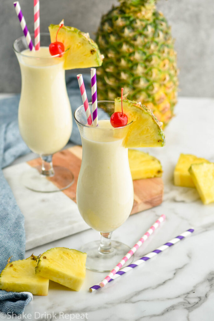 Two glasses of pina colada with straws, pineapple wedge and cherry