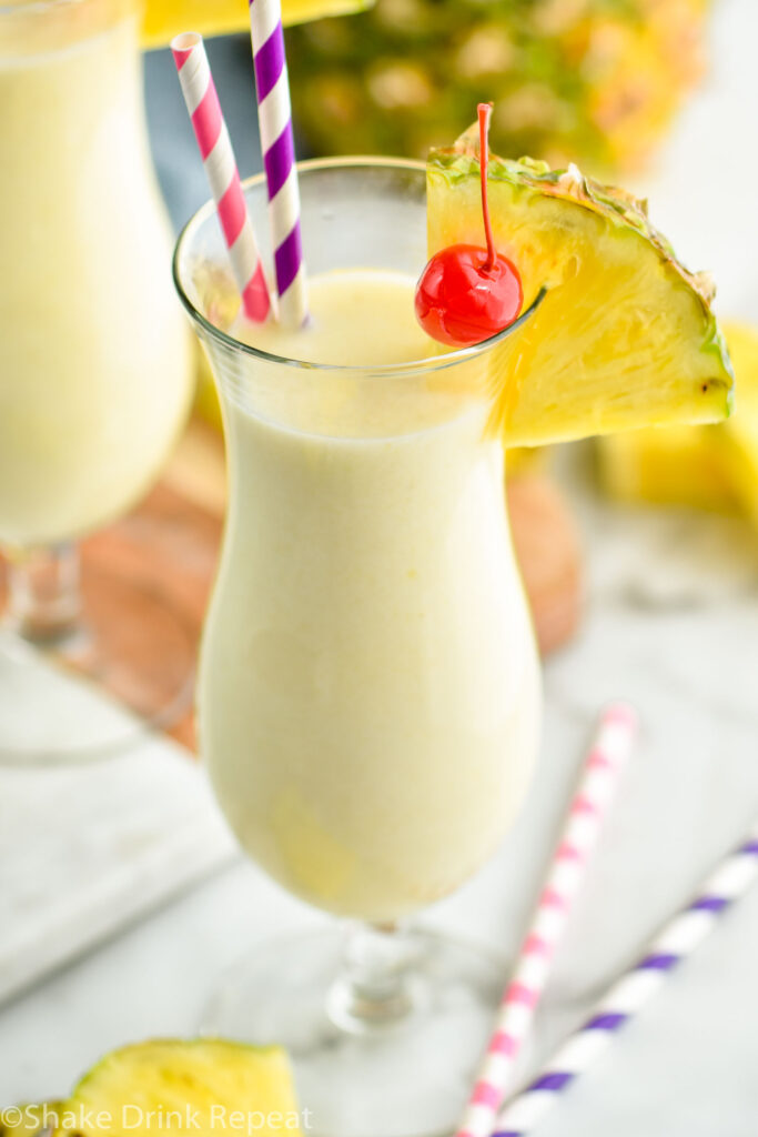 glass of pina colada with straws, pineapple wedge, and cherry