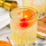 Two glasses of amaretto sour with ice, orange slice, and cherry garnish