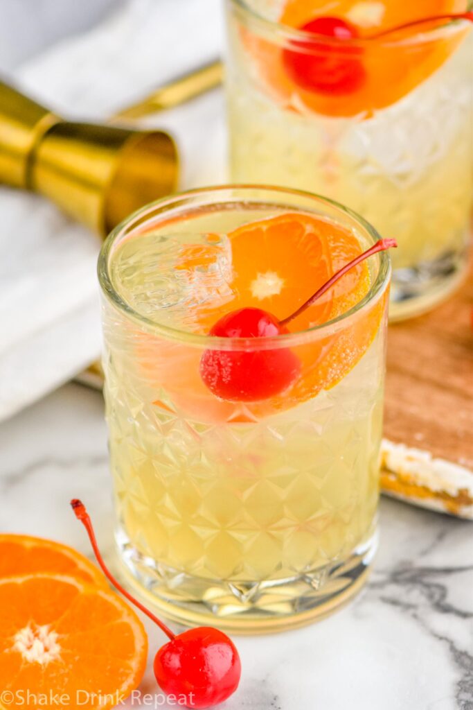 Two glasses of amaretto sour with ice, orange slice, and cherry garnish