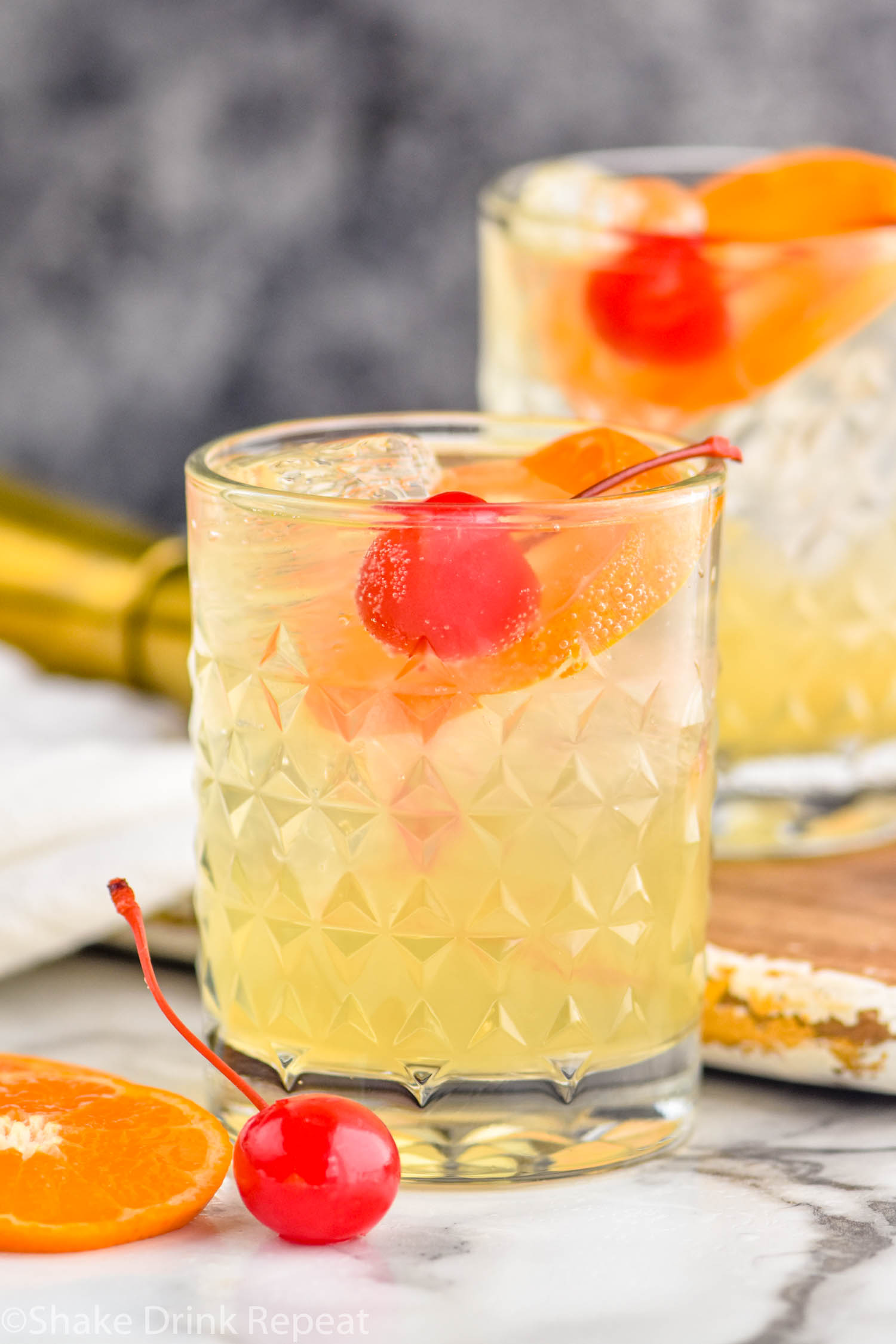two glasses of Amaretto Sour with ice, orange slices, and cherry garnish