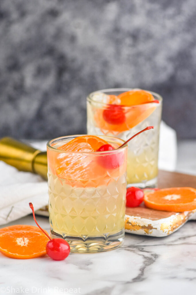two glasses of amaretto sour with ice, orange slices and cherries