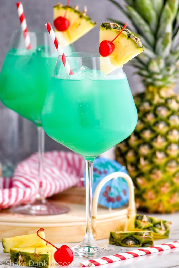 two glasses of blue hawaii with ice, straws, pineapple, and a cherry