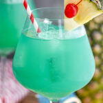 glass of blue hawaii with ice, a straw, pineapple, and a cherry