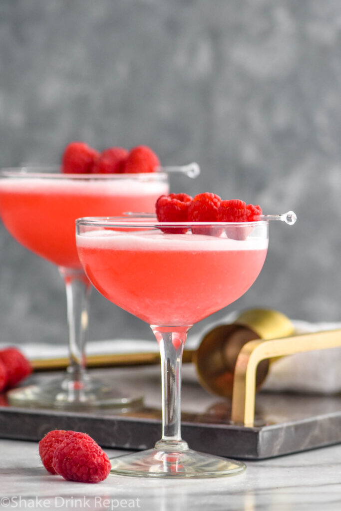 two glasses of clover club cocktail with raspberry garnish