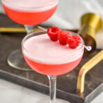 two glasses of clover club cocktail with raspberry garnish