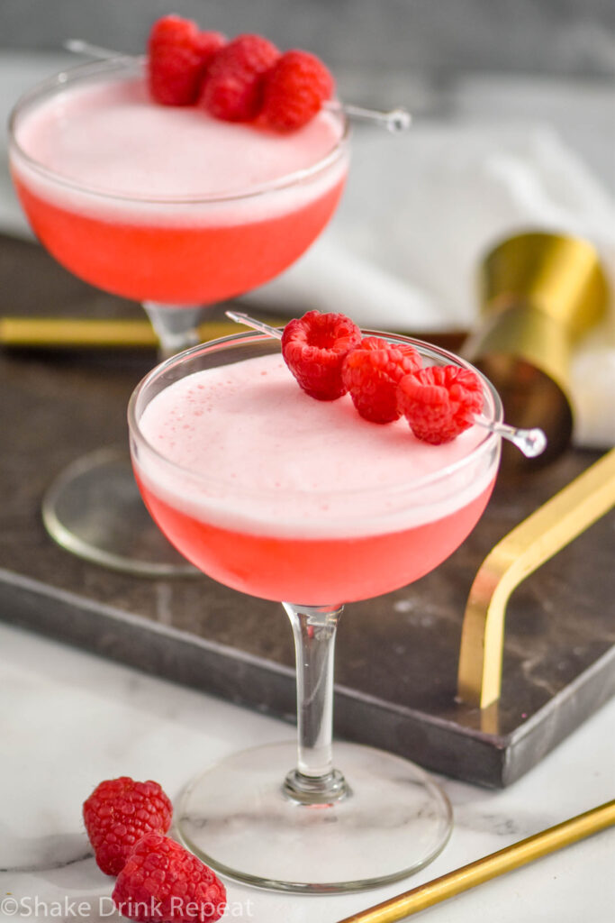 two glasses of clover club cocktail with raspberry garnish