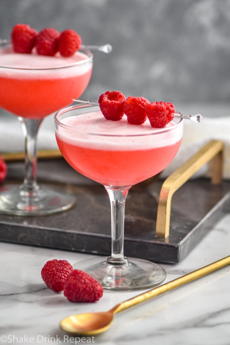 two glasses of clover club cocktail with raspberry garnish and gold spoon