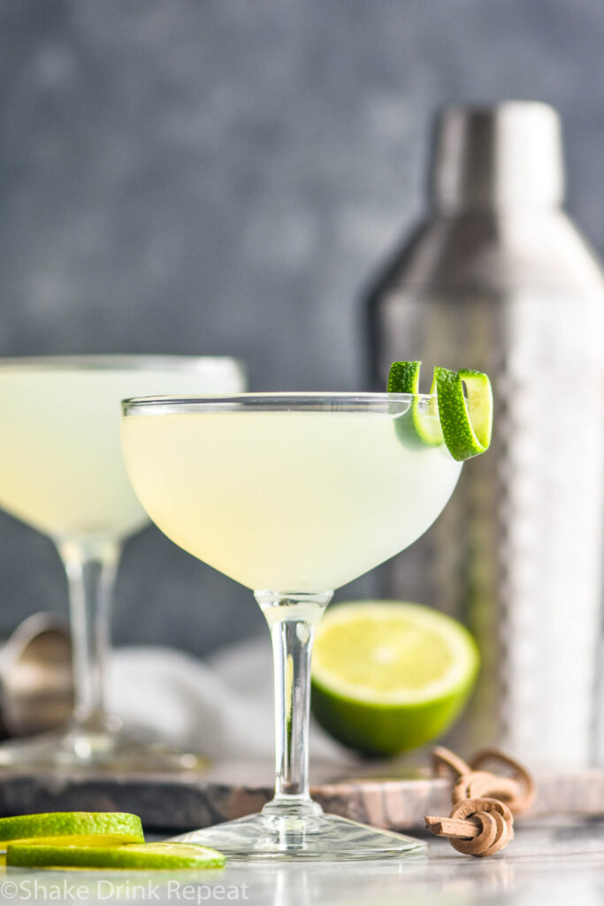 two cocktail glasses of daiquiri with lime twist and shaker in the background