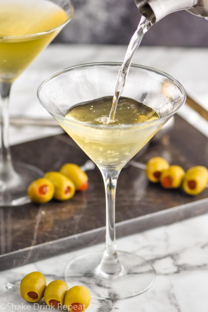 making a dirty martini in a glass with green olives