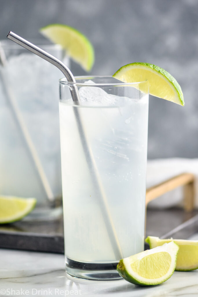 two glasses of gin rickey with ice, straws, and lime wedge garnish