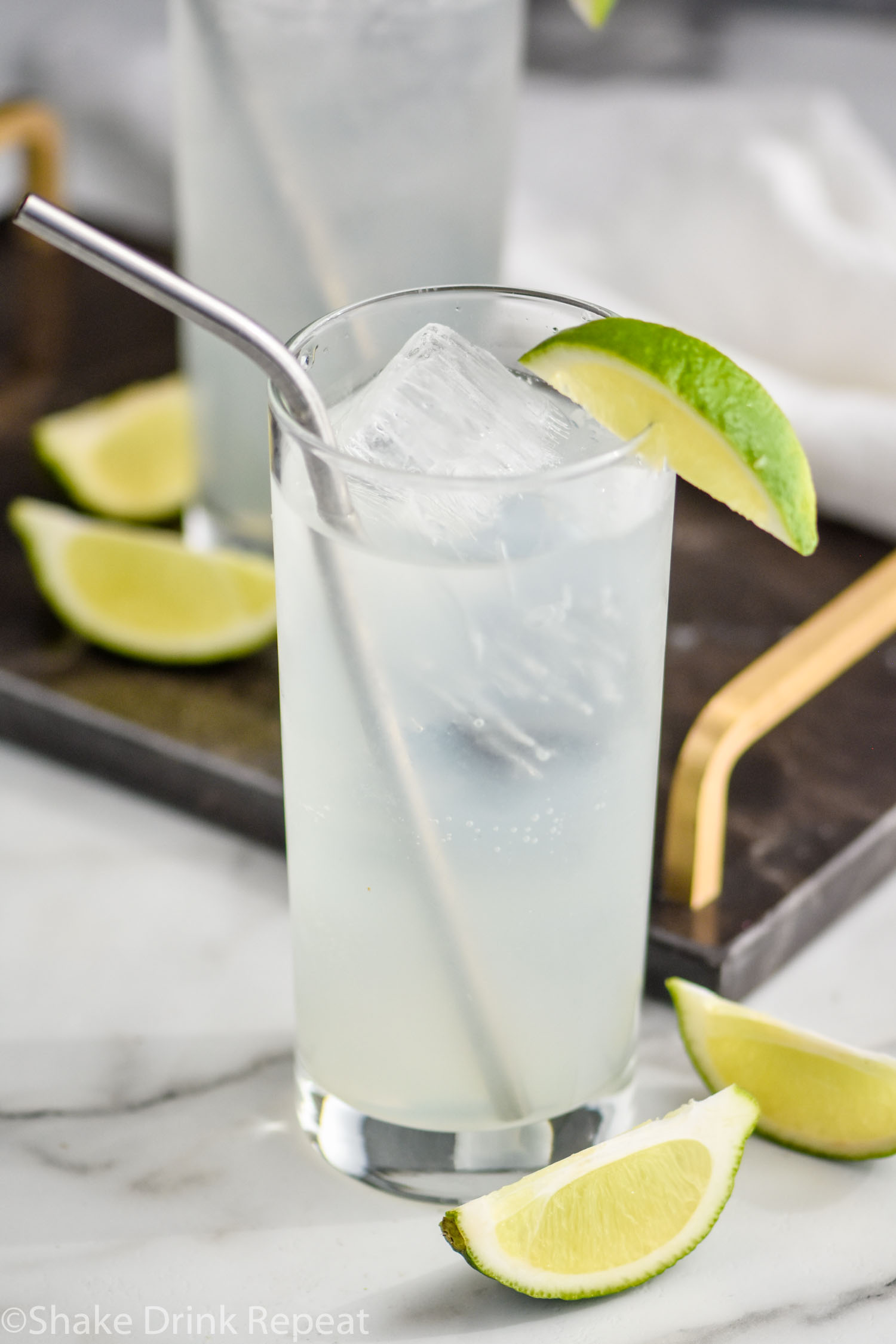 glass of gin rickey with ice and straw surrounded by lime wedges