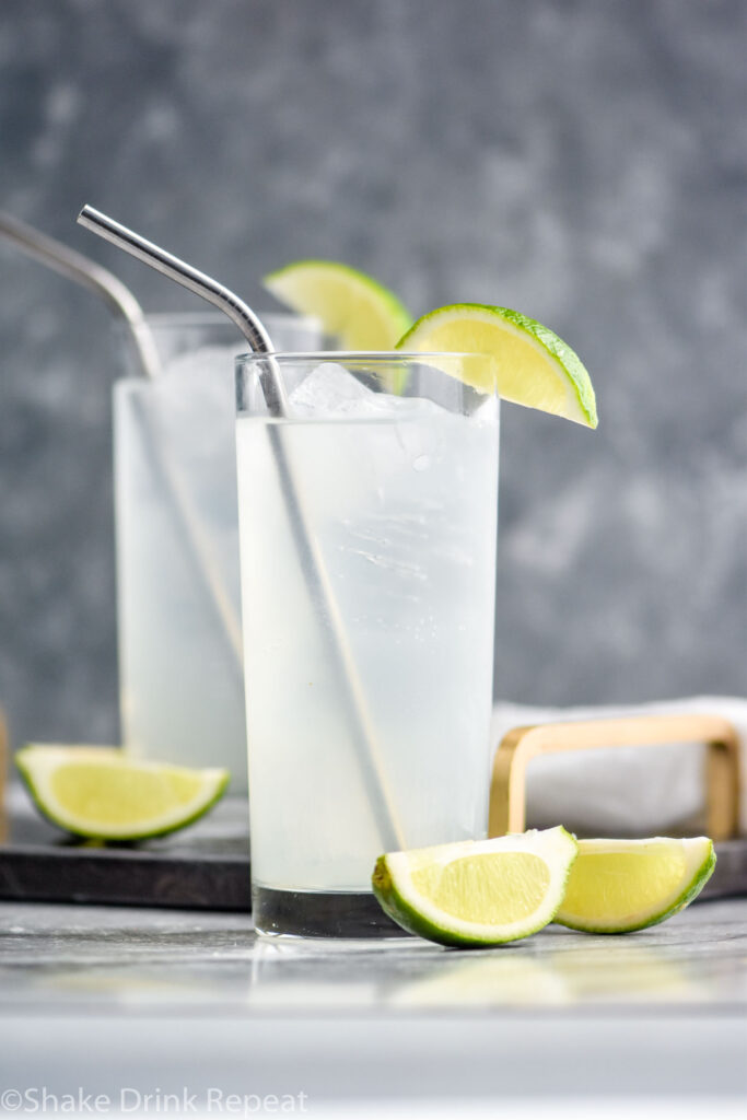 two glasses of gin rickey with ice, straws, and lime wedges