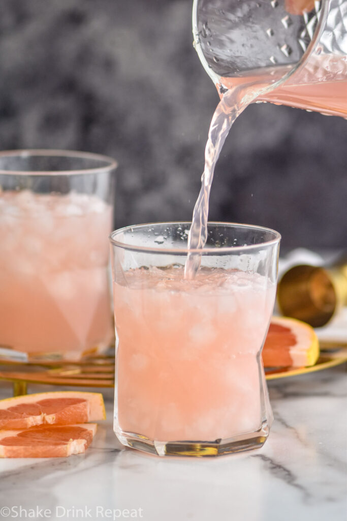 two glasses of paloma cocktail poured from a pitcher with crushed ice and grapefruit