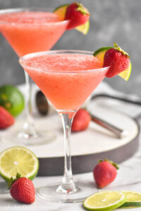 two glasses of strawberry daiquiri with fresh strawberries and limes