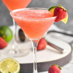two glasses of strawberry daiquiri with fresh strawberries and limes