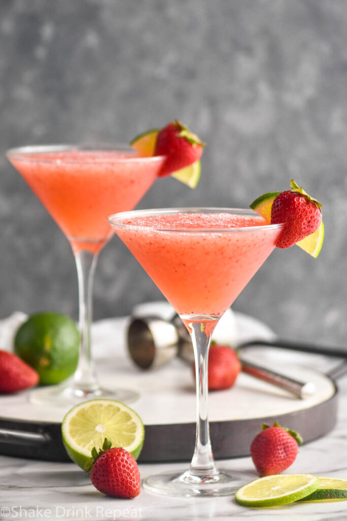 two glasses of strawberry daiquiri with fresh limes and strawberry garnish