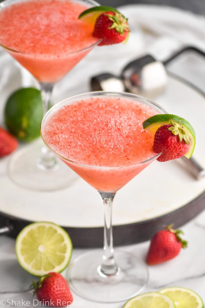 two glasses of strawberry daiquiri with fresh limes and strawberries