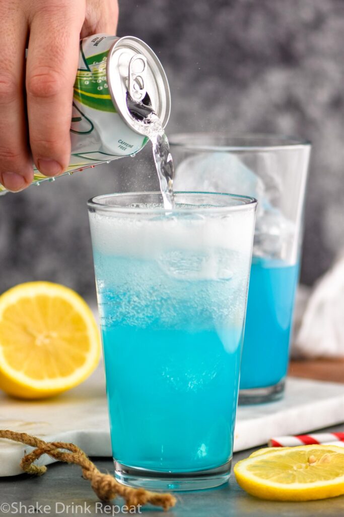 man pouring 7up into a glass of walk me down cocktail with lemons and ice