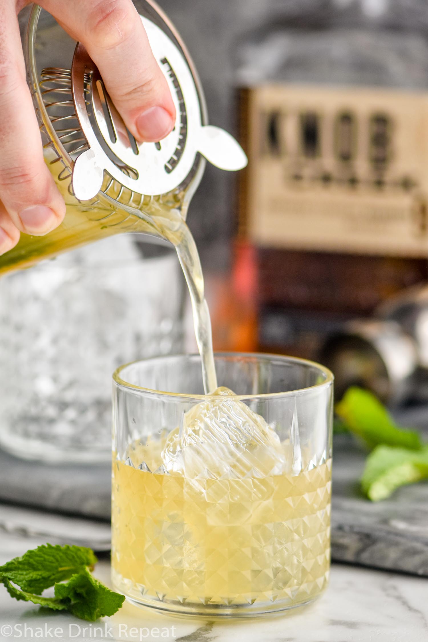 pouring a whiskey smash into a glass with ice and fresh mint